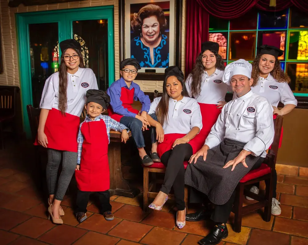 Domenic Laurenzo and his family in El Tiempo uniforms, seated beneath a portrait of Mama Ninfa